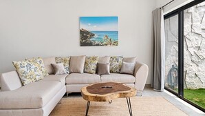 A modern living room with a beige sectional sofa, a wooden coffee table, and a large window with a stone wall. - Quiet La Punta Surf Villa (Santa María Colotepec)
