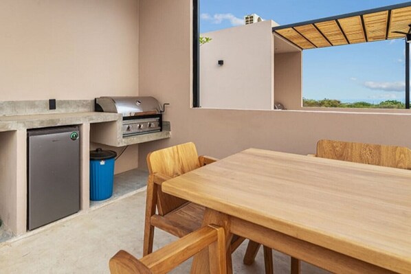 Una cocina exterior compacta con una parrilla empotrada, un refrigerador pequeño y un cubo de basura.