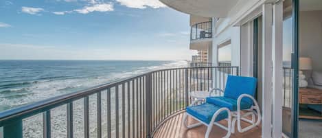 A balcony with a view of the ocean, a blue chair, and a patterned rug.