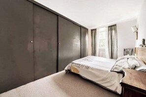 Cozy retreat with a comfortable bed, dark wardrobe, and a bedside table with a lamp.
