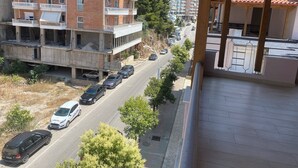 Un immeuble à plusieurs étages doté de balcons, une rue bordée de voitures garées et une vue dégagée sur les environs.