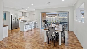 Eine moderne Küche mit weißen Schränken, einem Edelstahlkühlschrank und einem Essbereich mit Holztisch und -stühlen.