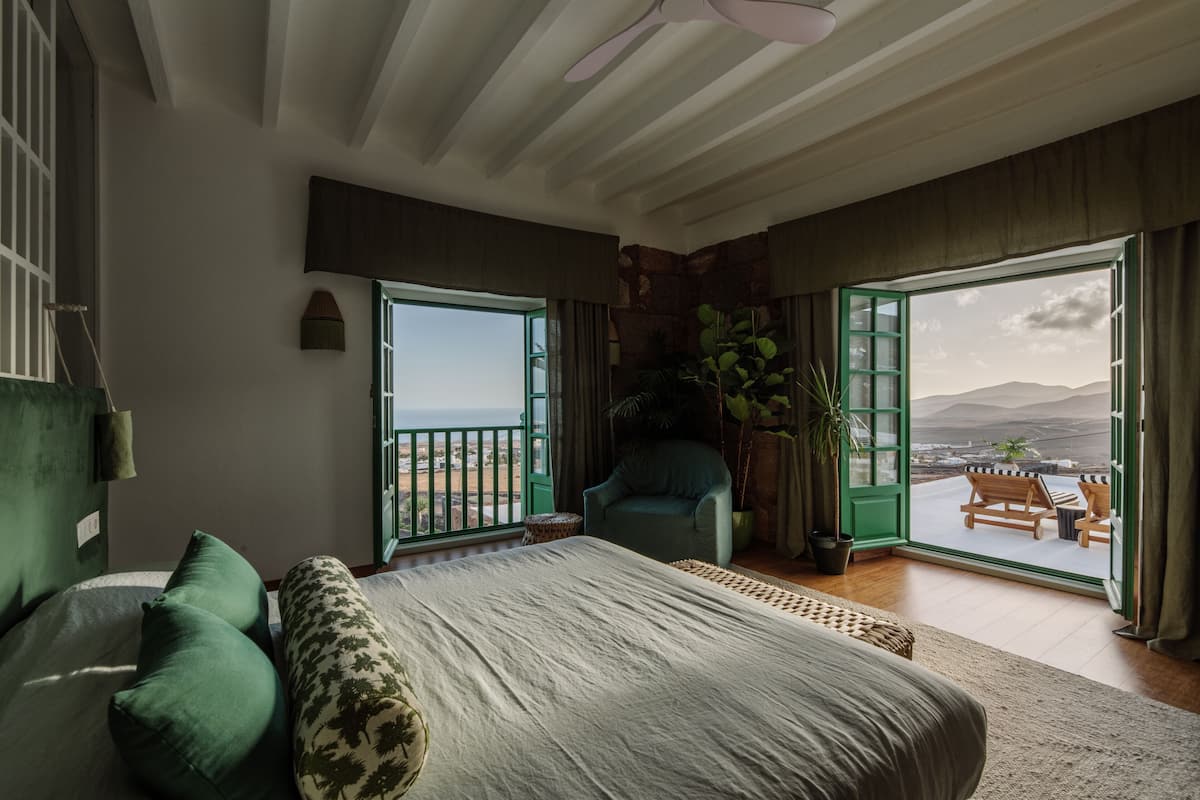 Un dormitorio con una cama grande, dos ventanas, una silla y un balcón con vistas.