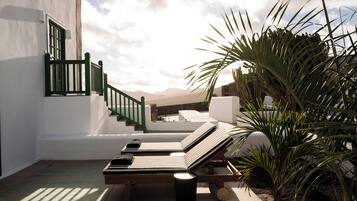 A sunlit outdoor seating area with two lounge chairs, a small trash bin, and a potted plant.