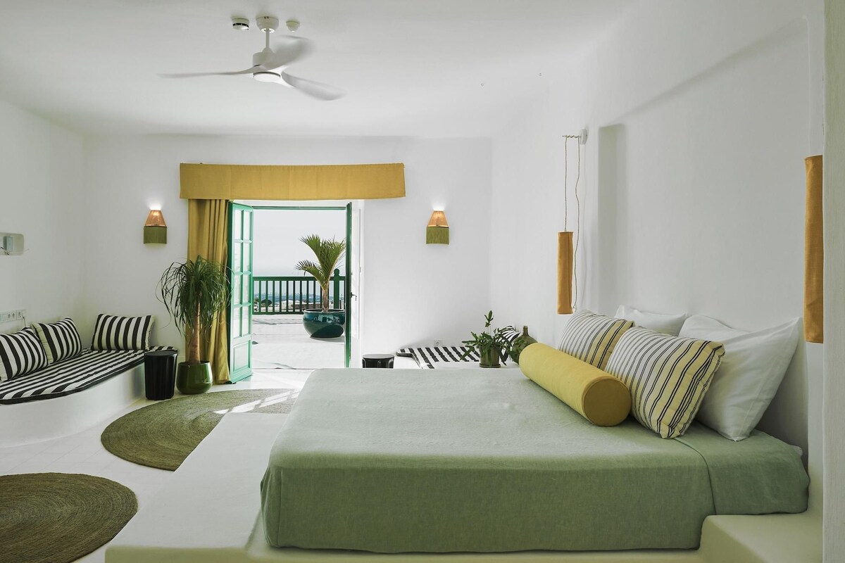Un dormitorio con cama, una zona de estar con sofá, ventilador de techo y vistas a través de una puerta abierta.