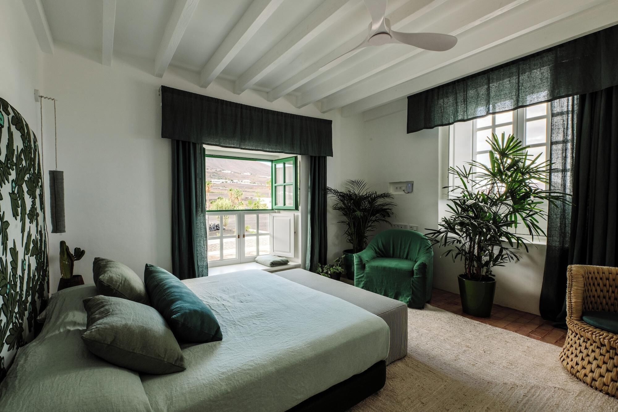 Un dormitorio con cama, una silla, una planta en maceta y una ventana con cortinas.