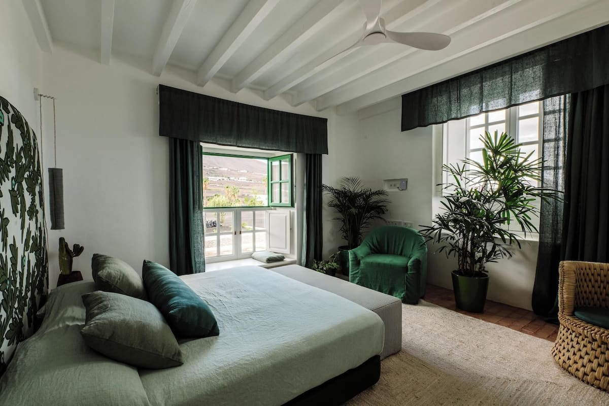 Un dormitorio con cama, una silla, una planta en maceta y una ventana con cortinas.