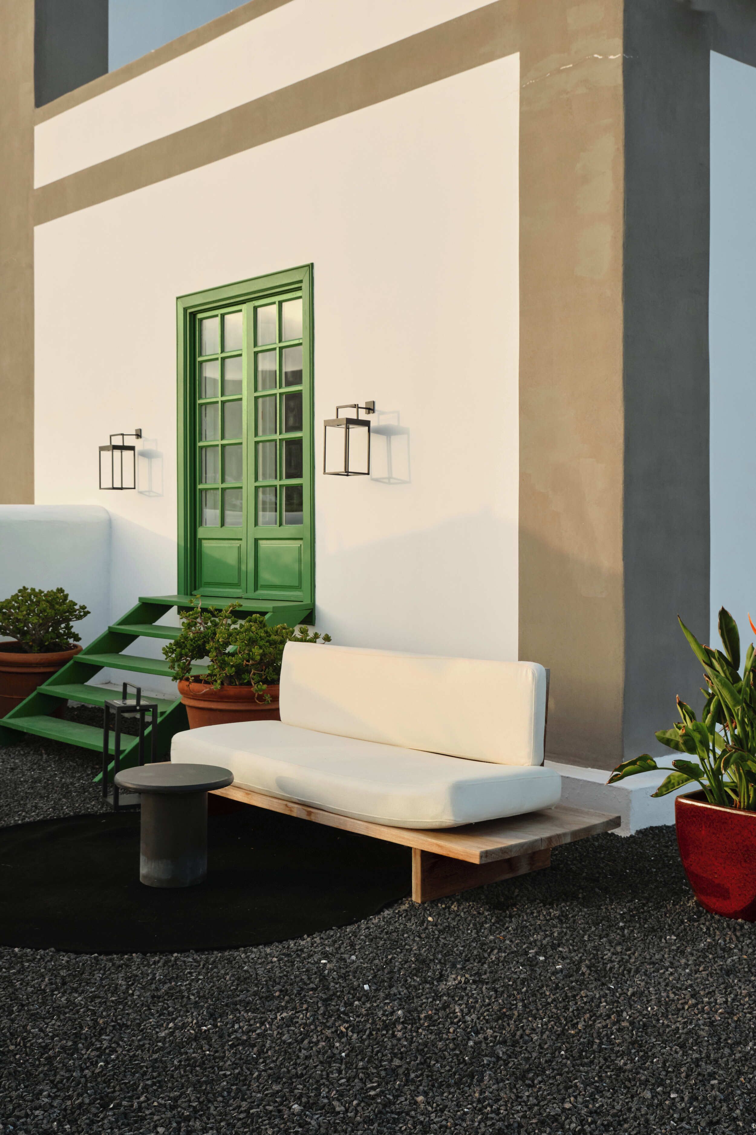 A white outdoor seating area with a green door, potted plants, and wall-mounted lights.