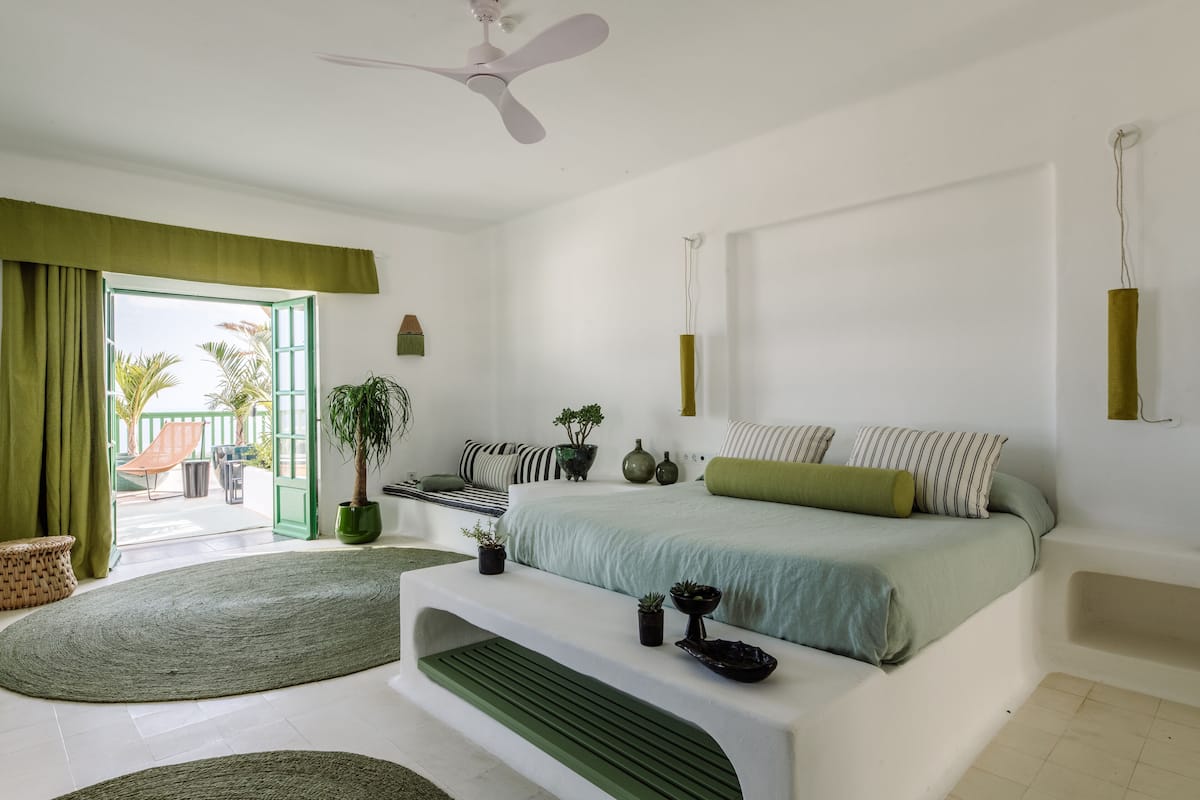 Un dormitorio moderno con cama, detalles en verde, ventilador de techo y vistas al exterior.