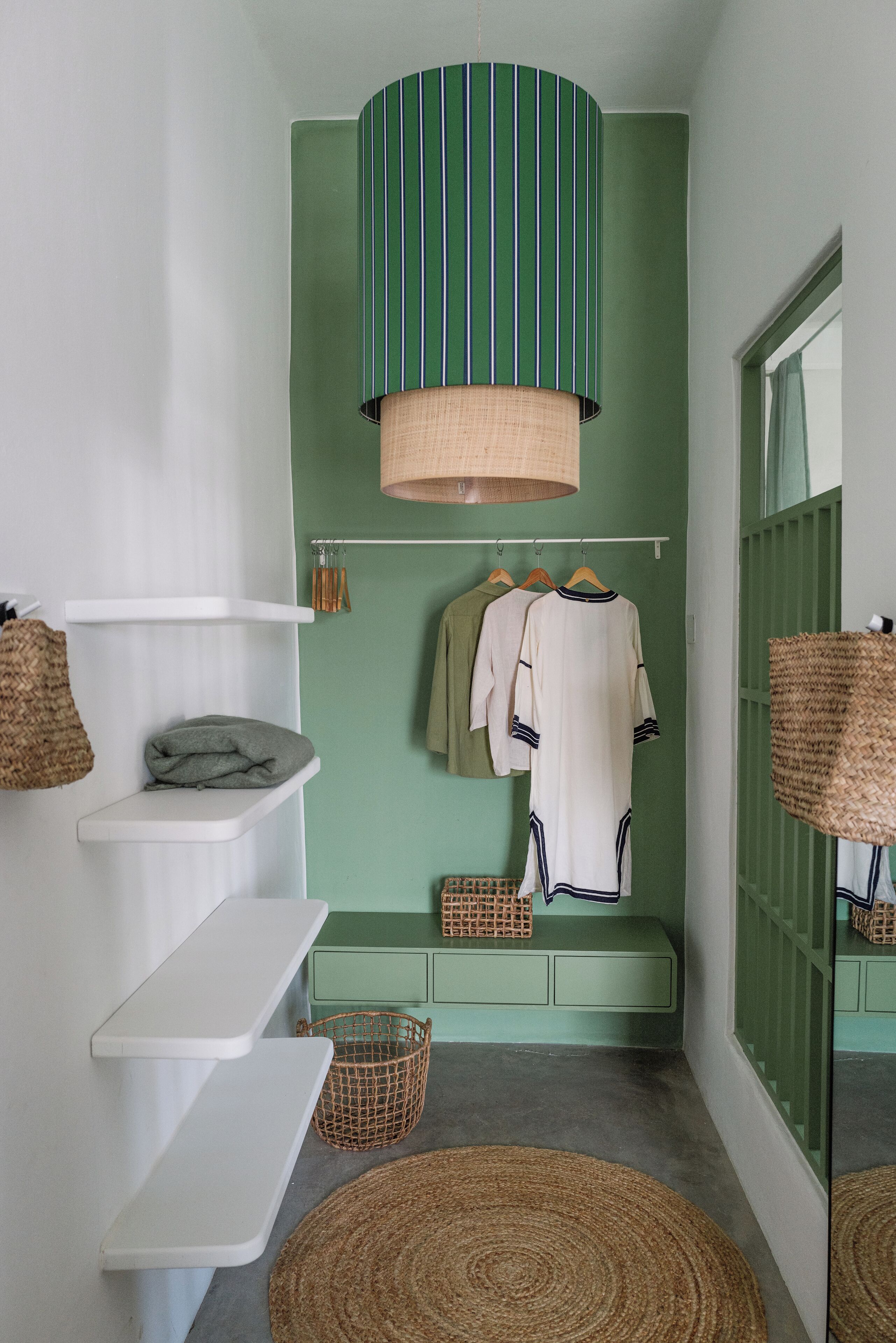 Un baño pequeño con pared verde, una lámpara colgante verde a rayas y un estante blanco con toallas.