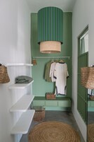 Un baño pequeño con pared verde, una lámpara colgante verde a rayas y un estante blanco con toallas.