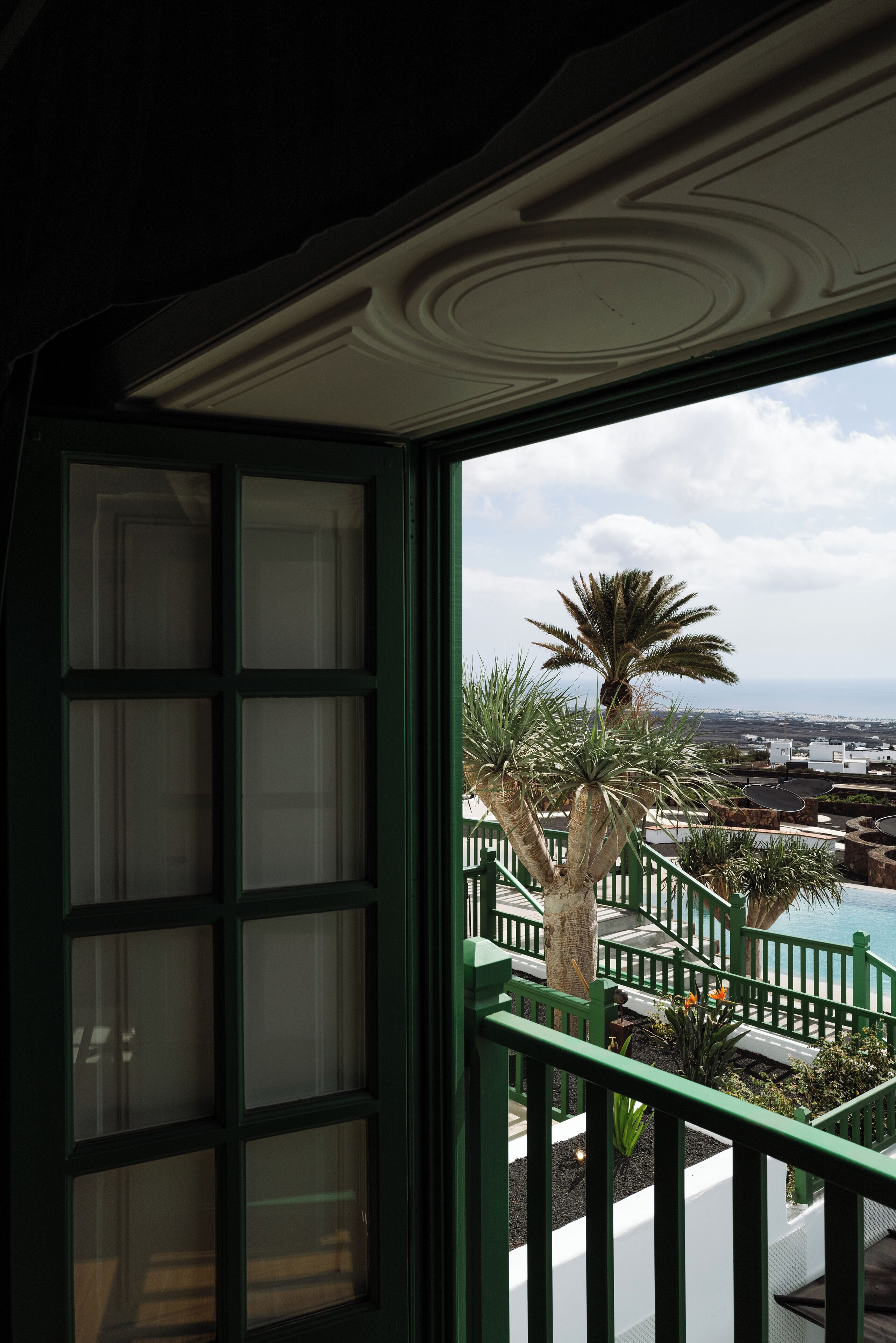 A view from a balcony with a green railing, a palm tree, and a pool area.