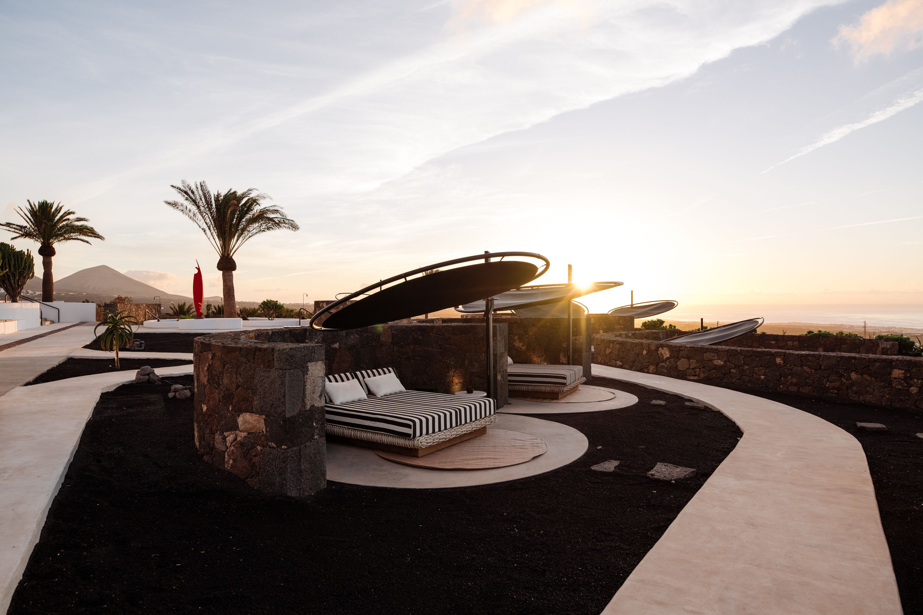 A modern outdoor lounge area with circular seating and a view of a mountain at sunset.
