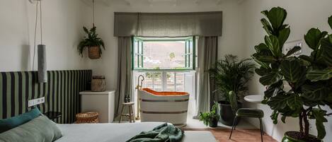 A modern bedroom with a large bed, a bathtub, and a view of the outdoors.