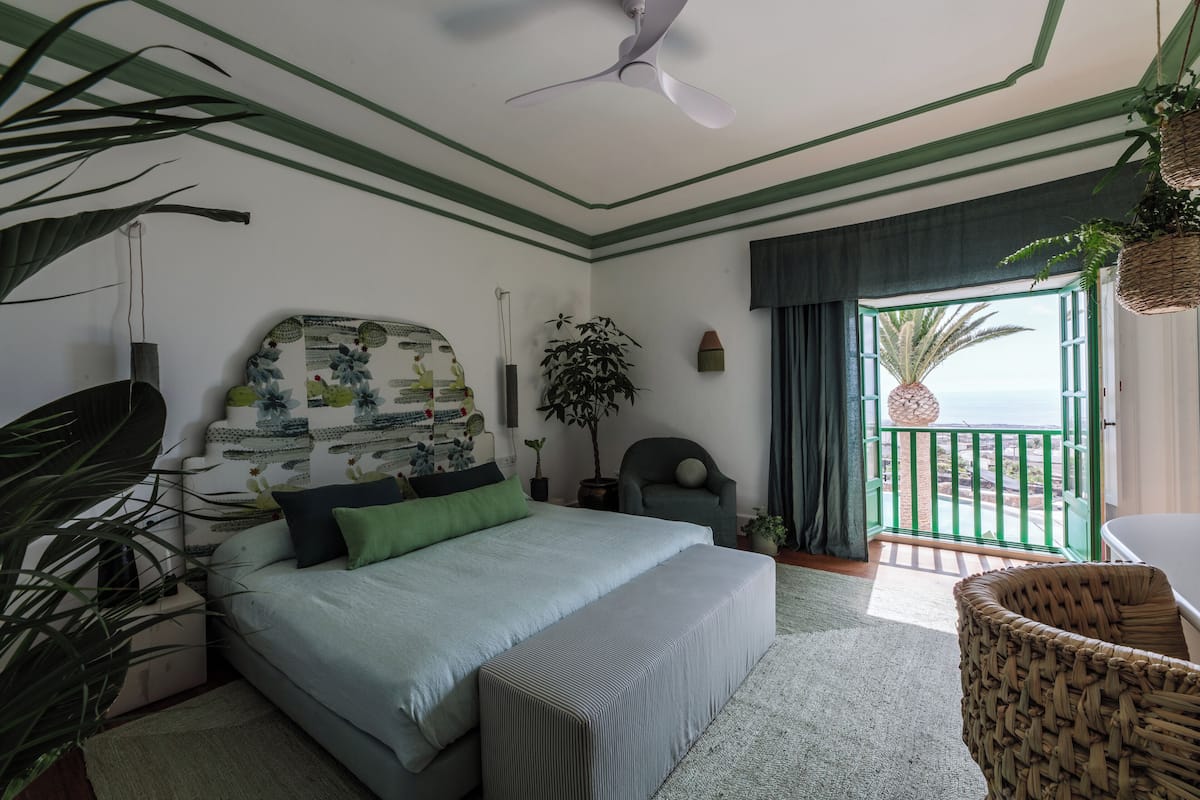 Un dormitorio con cama, una silla, una planta en maceta y vista al océano.