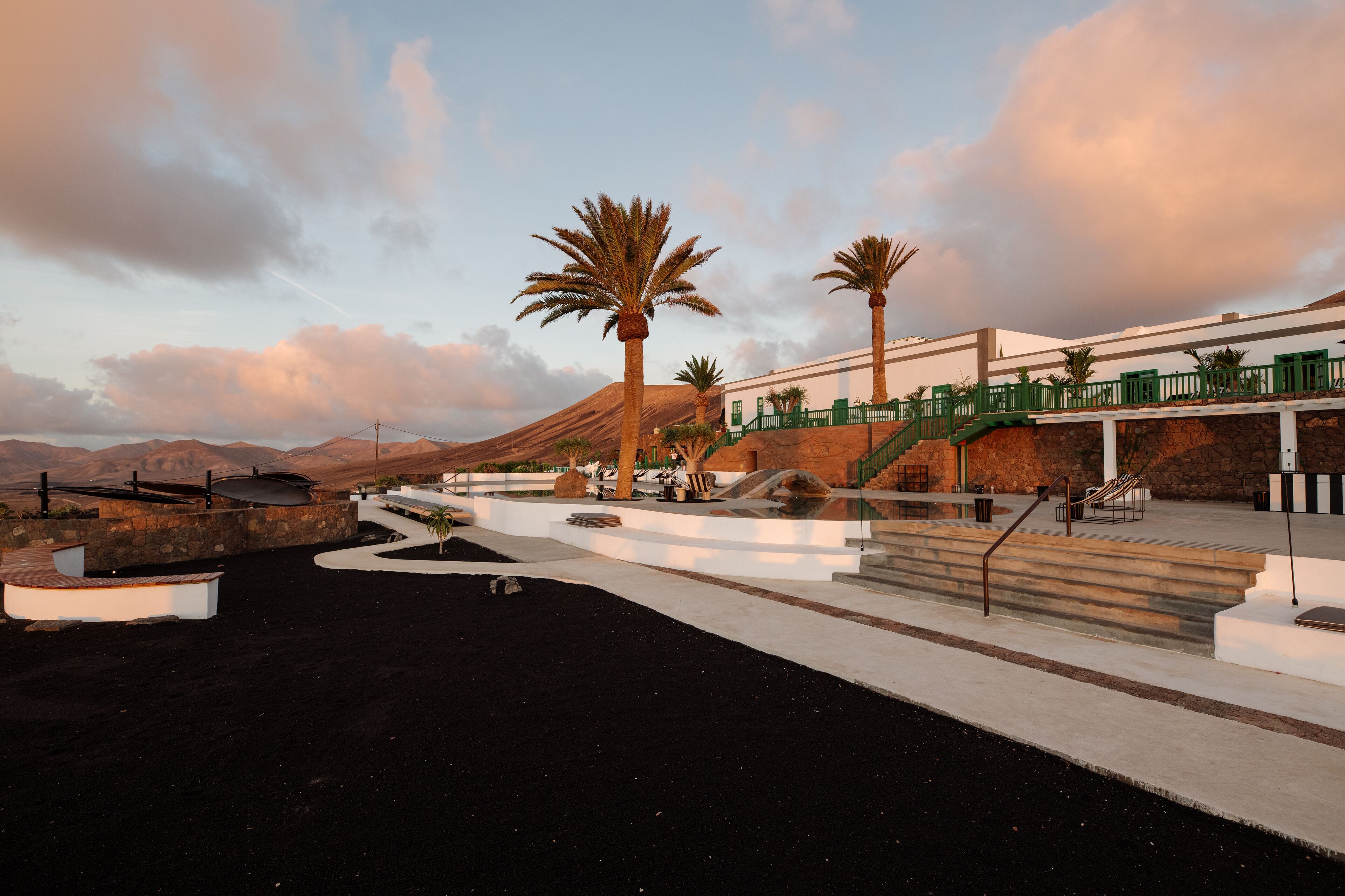 Un hôtel moderne avec un chemin en béton, des palmiers et une montagne en arrière-plan.
