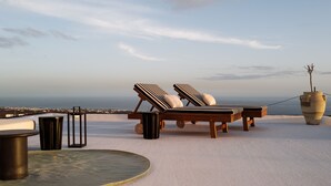 A rooftop lounge with two sun loungers, a round table, and a potted plant.