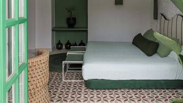 Un dormitorio con una cama, almohadas verdes, una planta en maceta, un estante con adornos y un suelo estampado.