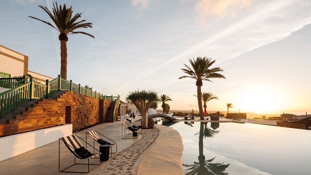 A serene pool area with a clear sky, palm trees, and a staircase leading to a building.