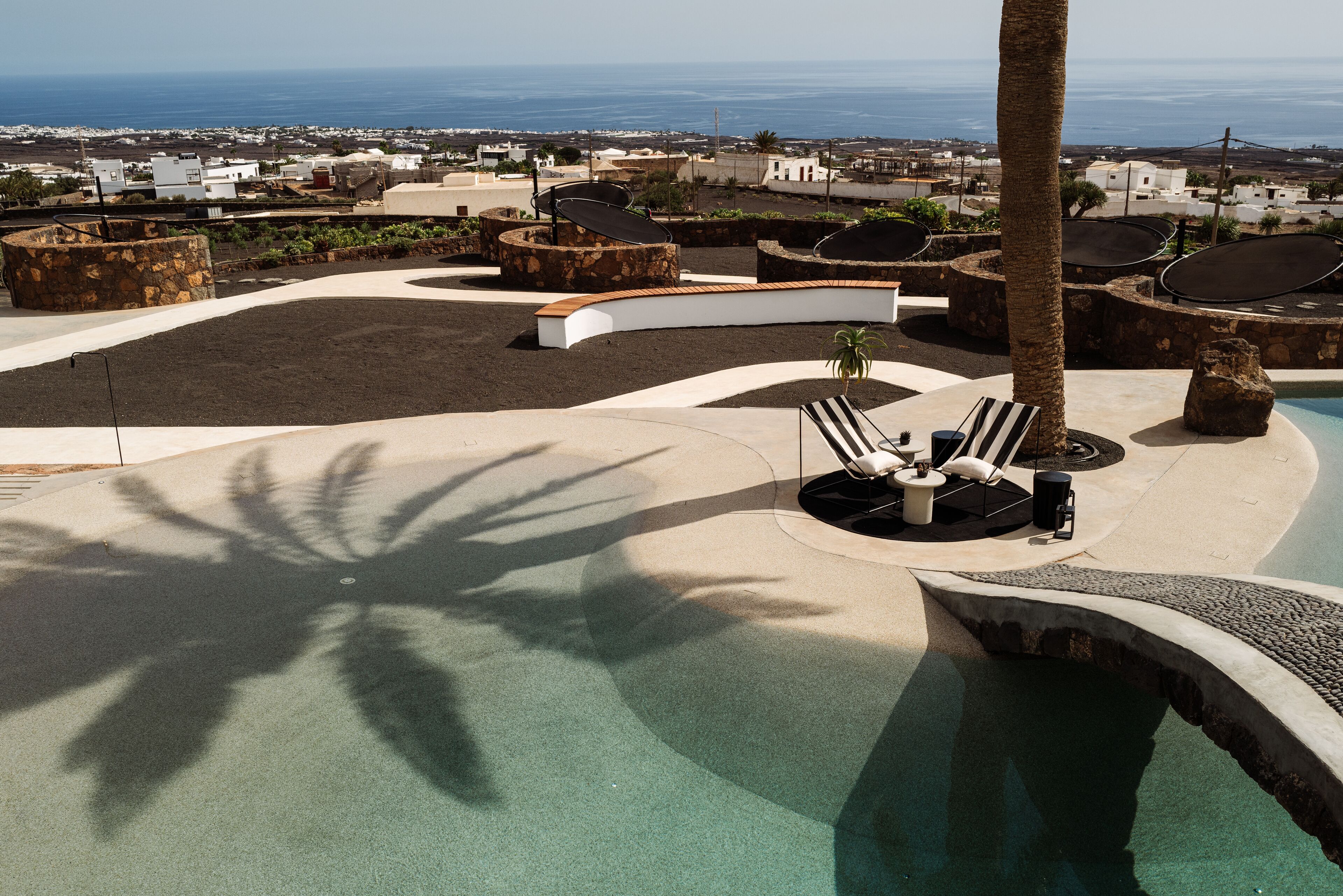 Área de piscina en la azotea con sillones, una palmera y vistas al océano y la ciudad.