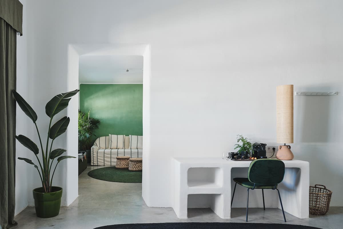 Una habitación moderna con un escritorio blanco, una silla verde, una planta en maceta y una pared verde de fondo.