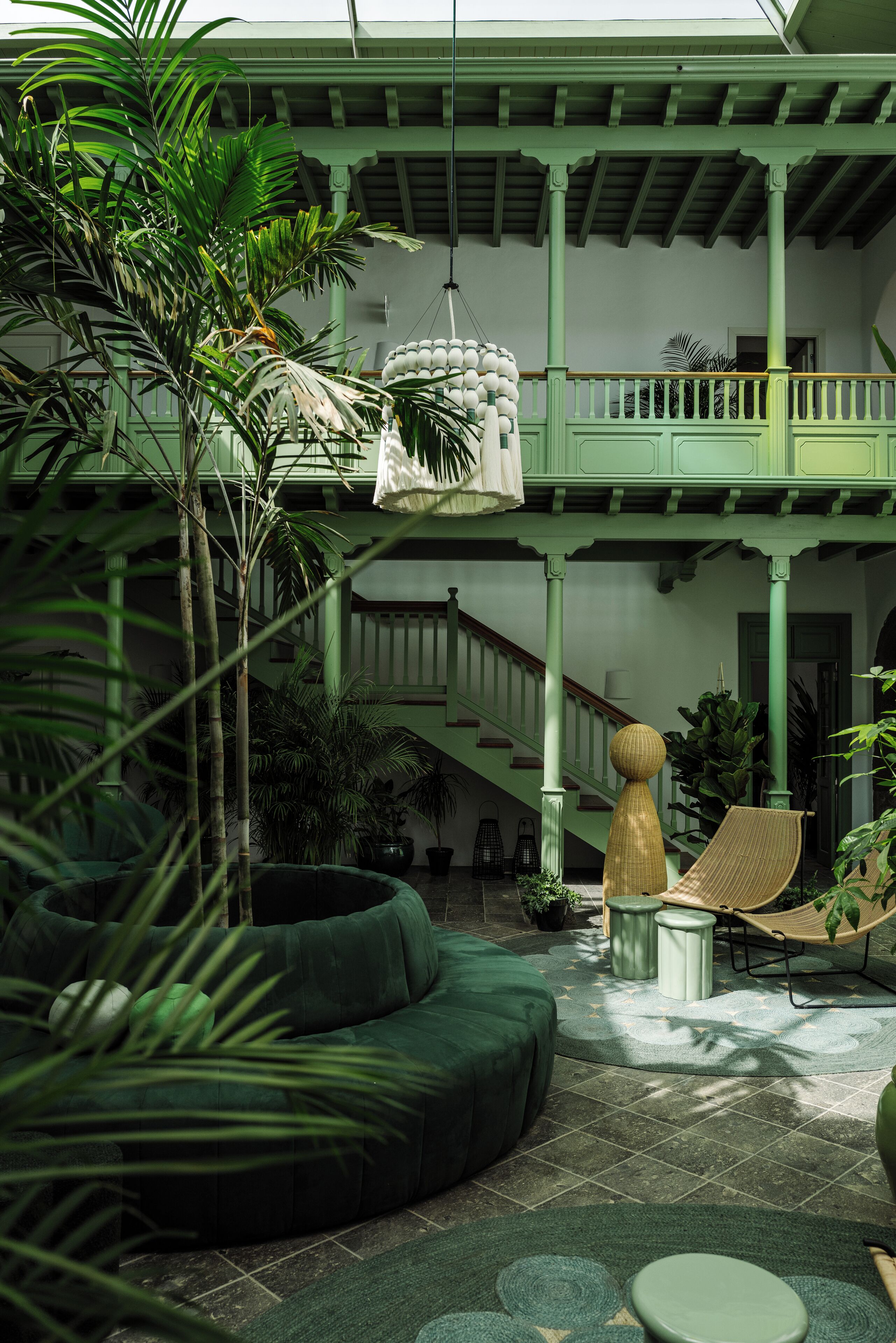 A spacious indoor courtyard with a green color scheme, featuring a hammock, a round green sofa, and a staircase leading to an upper level.