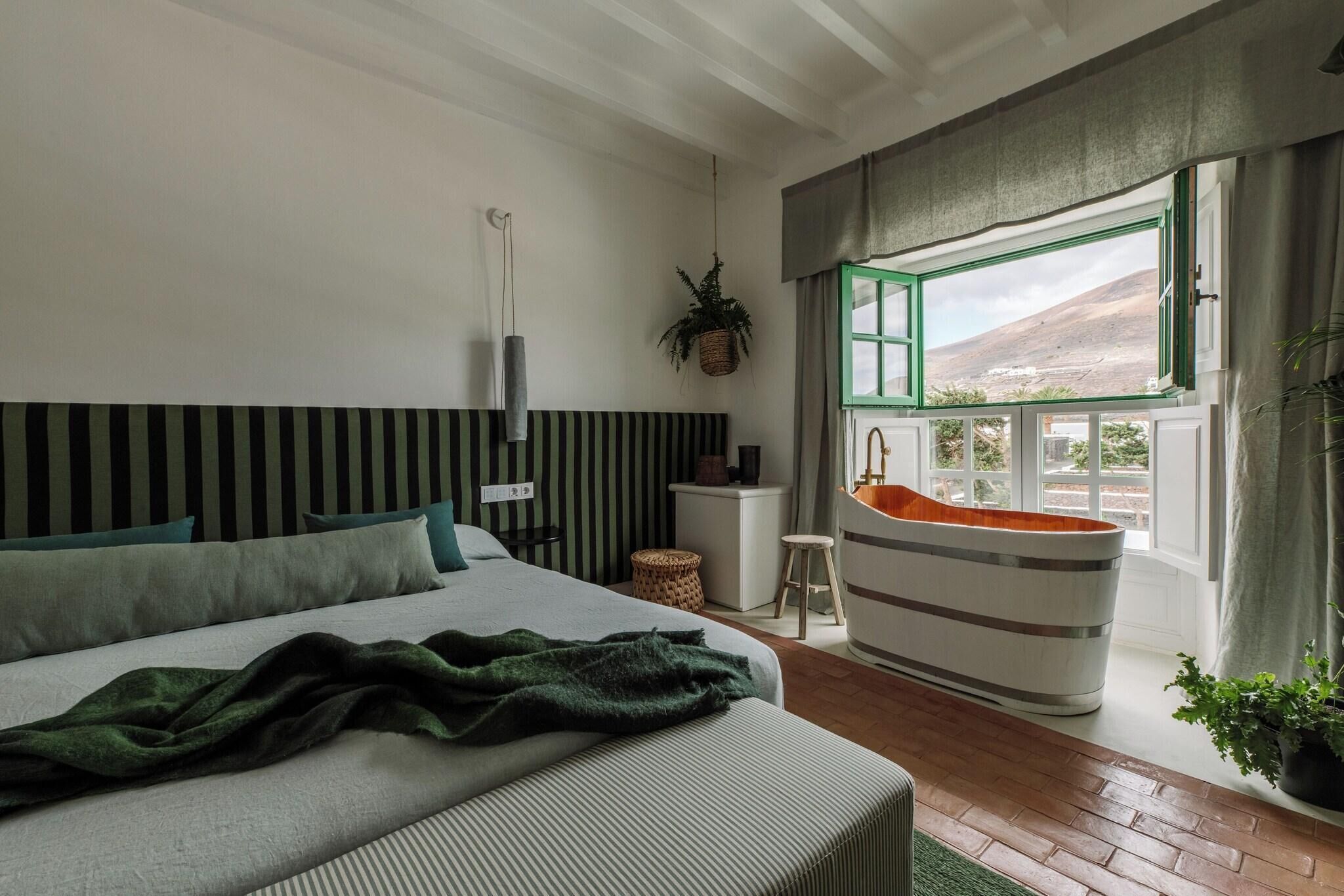 Un dormitorio con una cama grande, una planta colgante, una bañera y vistas a la montaña.