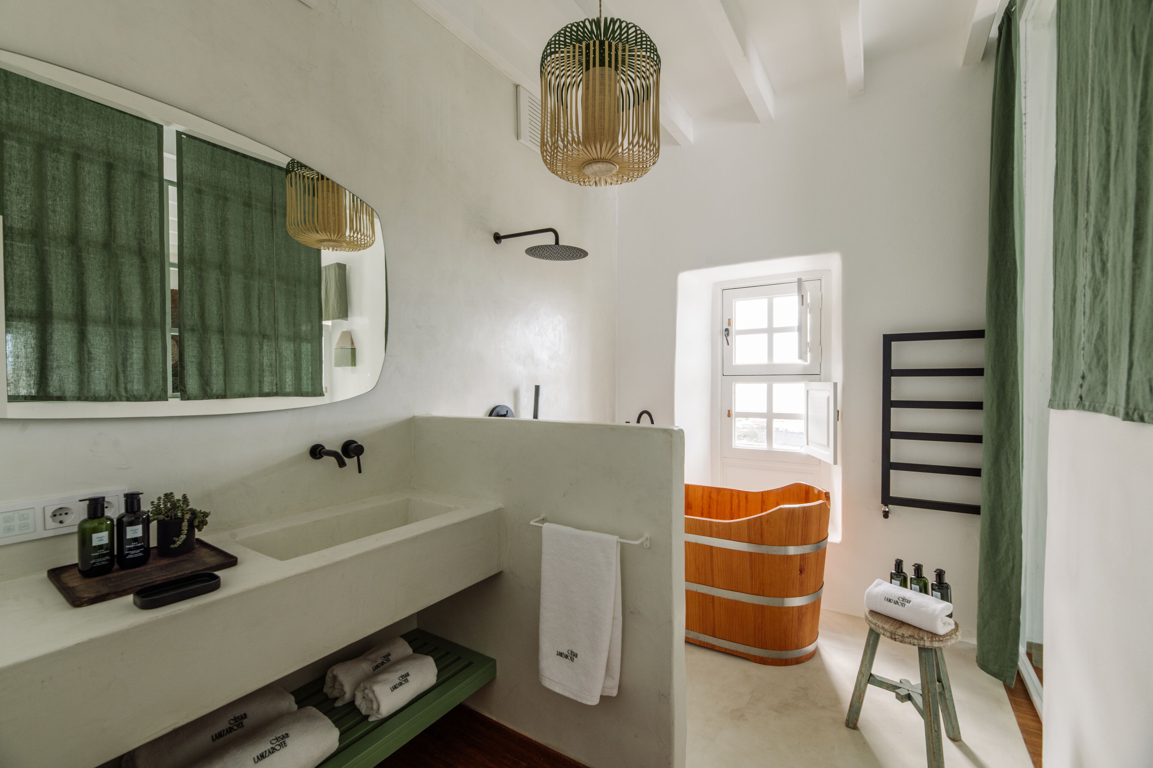 Un baño con un lavamanos grande, un espejo, una ducha, un barril de madera y un taburete pequeño.