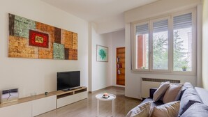Een moderne woonkamer met een flatscreen televisie, een salontafel, een bank en een groot abstract schilderij aan de muur.