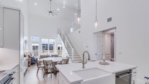 Una cocina moderna con una isla central, un comedor con sillas de madera y una escalera que sube a un nivel superior.