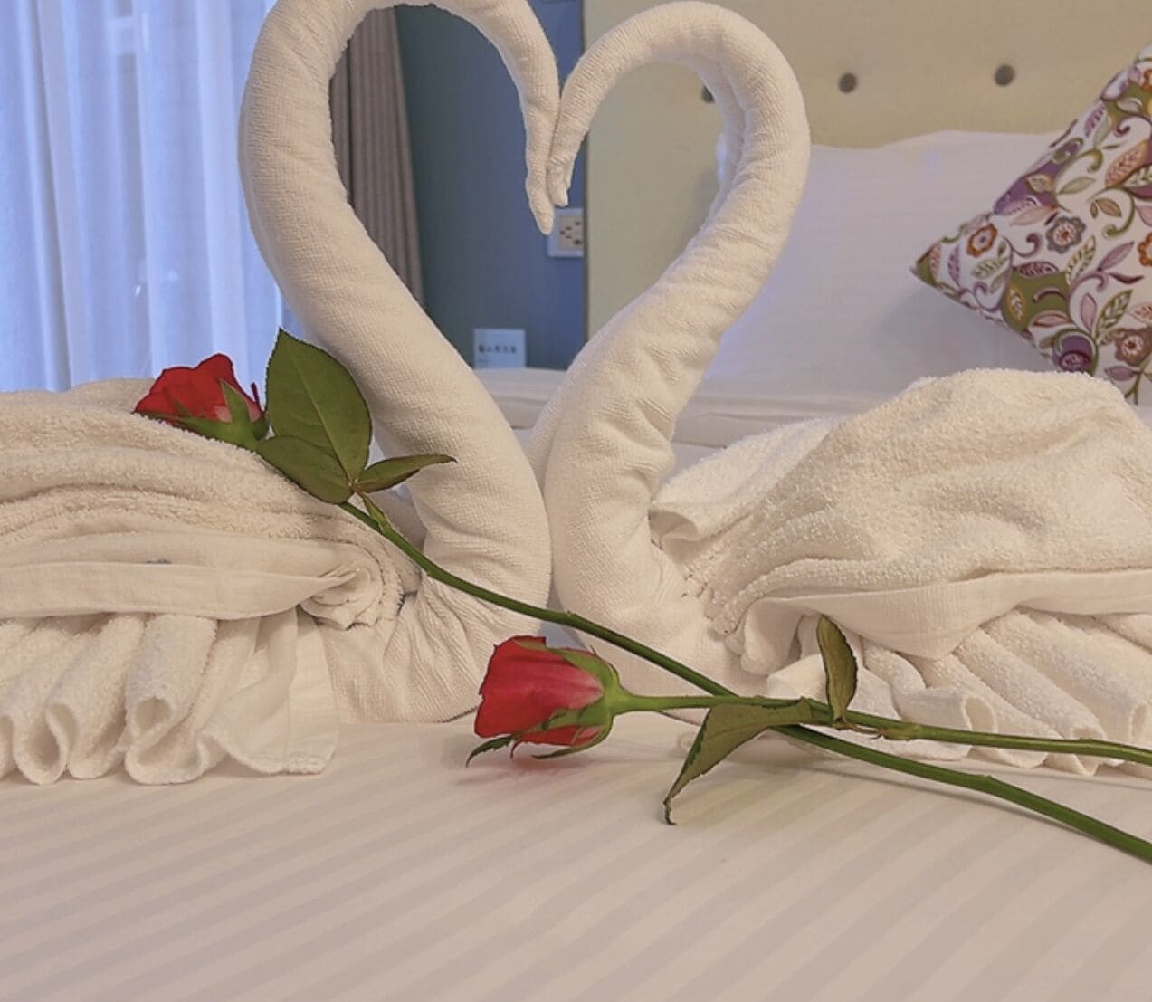 Een bed met een handdoek in de vorm van een hart en een enkele rode roos.