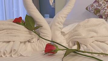 Een bed met een handdoek in de vorm van een hart en een enkele rode roos.