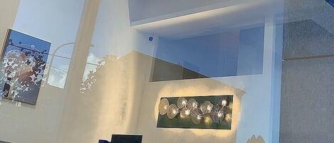 Una sala de estar moderna con techo alto, una araña, una zona de comedor con mesa y sillas, y obras de arte en las paredes.