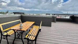 Una terraza en la azotea con una mesa y bancos de madera, un farol y vistas a montañas distantes bajo un cielo parcialmente nublado.