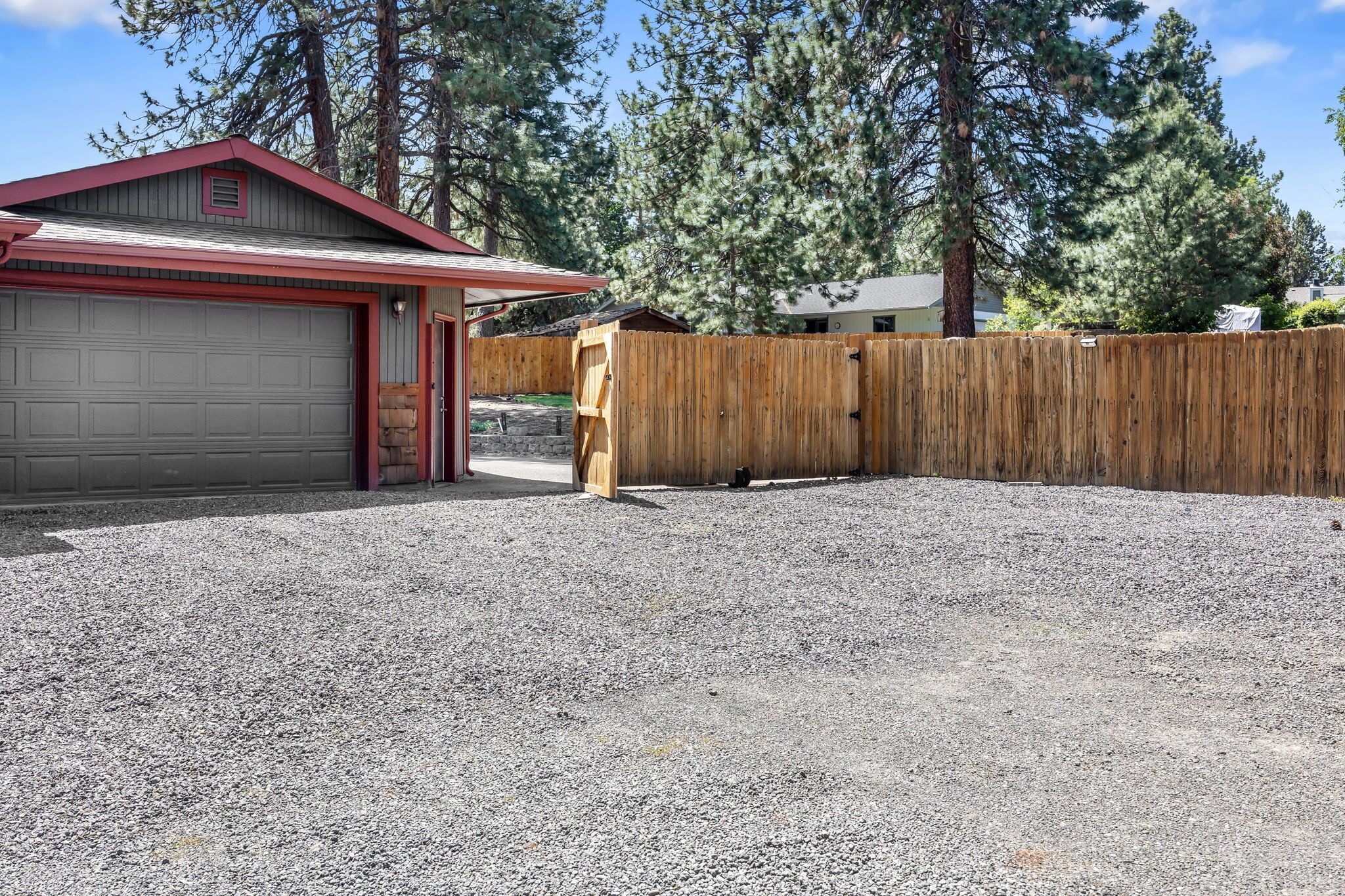A garage with a red roof, a wooden fence, and a gravel driveway.