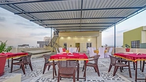 Una terraza al aire libre con mesas y sillas, un paseo cubierto y un edificio al fondo.