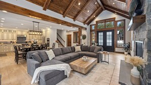 A spacious living area with a large sectional sofa, a coffee table, and a fireplace. The kitchen is visible in the background with wooden cabinets and a stone backsplash. - Family Time Comes First | Stay Longer w/ 1PM In/Out Benefits (Cle Elum)