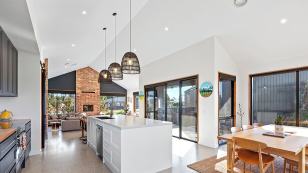 A modern kitchen with a central island, a dining area with a wooden table and chairs, and a large sliding glass door leading to a patio. - Buller Peeps  - Mansfield (Mansfield)