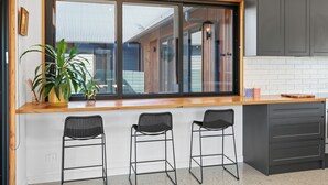 A kitchen with a large window, three bar stools, a potted plant, and grey cabinets. - Buller Peeps  - Mansfield (Mansfield)