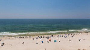 A wide beach with numerous umbrellas and beach chairs, a lifeguard tower, and a clear view of the ocean. - Lighthouse 1507 by Liquid Life (Gulf Shores)