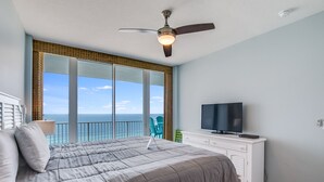 A bedroom with a bed, a ceiling fan, a TV, and a view of the ocean. - Lighthouse 1507 by Liquid Life (Gulf Shores)