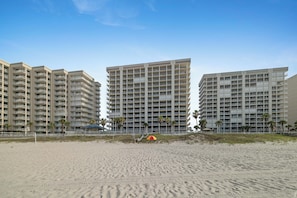 A beachfront hotel with multiple high-rise buildings, a sandy beach, and a small umbrella.