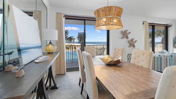A dining area with a wooden table, white chairs, and a view of the ocean through large windows. - Windward Pointe 201 by Liquid Life (Orange Beach)