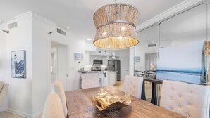 A dining area with a wooden table, cushioned chairs, and a decorative bowl centerpiece. - Windward Pointe 201 by Liquid Life (Orange Beach)