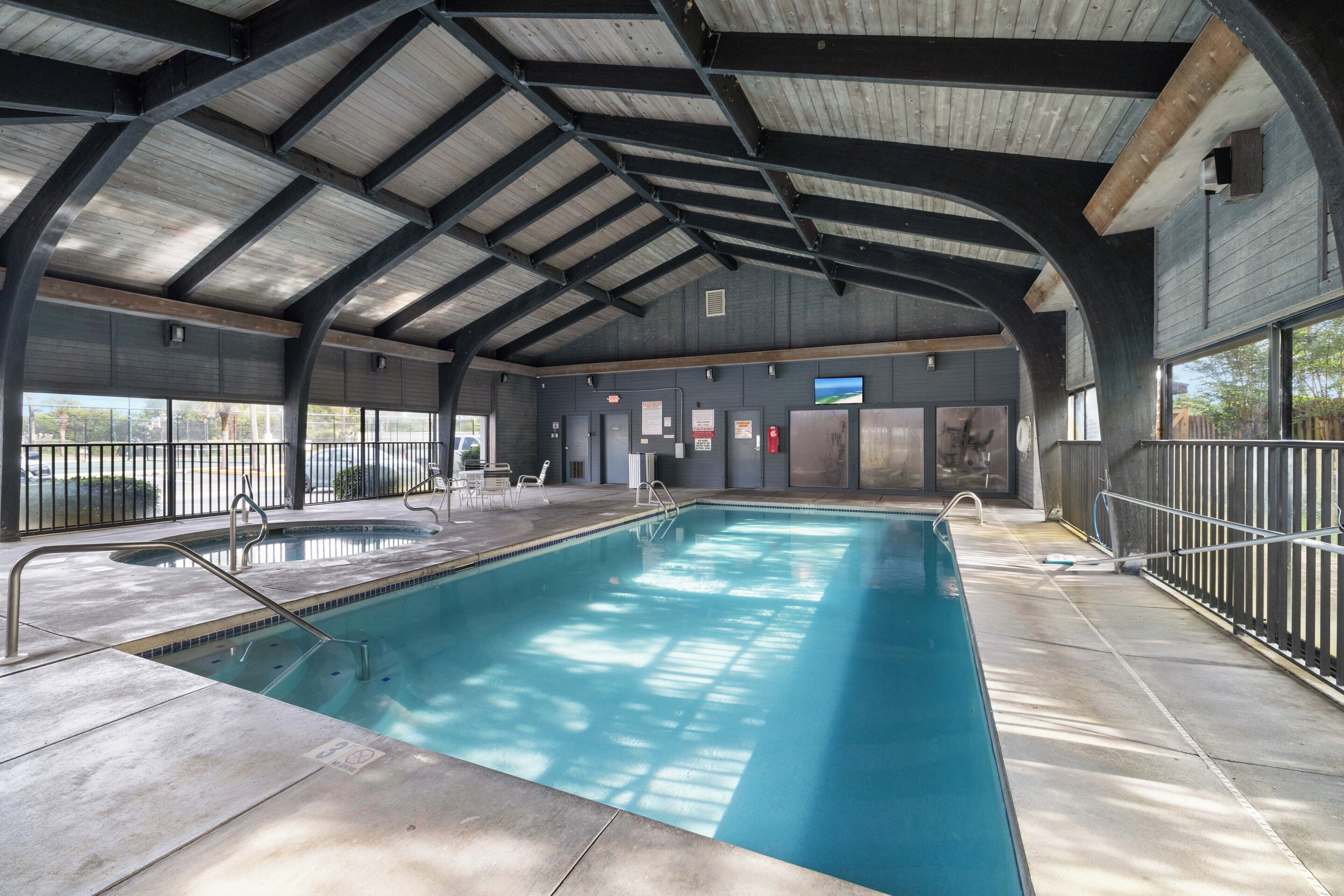 An indoor swimming pool with a high ceiling and metal beams, surrounded by a fenced area.