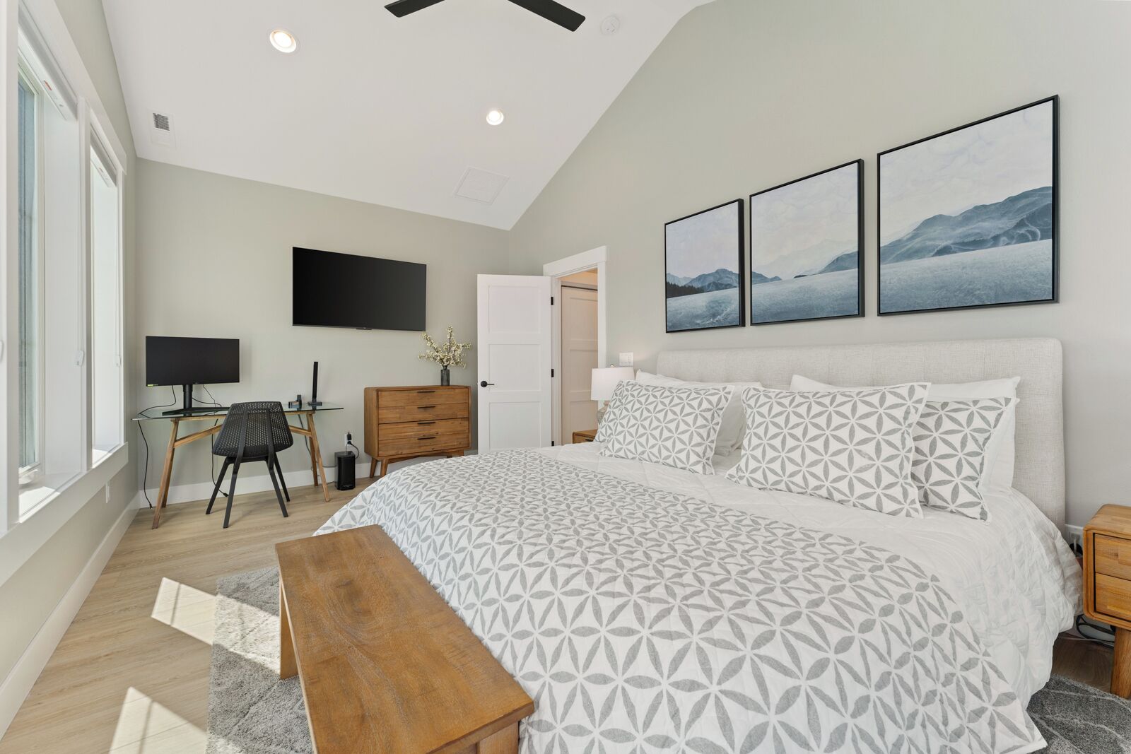 A bedroom with a large bed, a desk, a chair, and a TV on the wall.