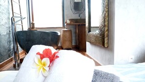 Une salle de bain avec une baignoire, une serviette ornée d’une fleur, une chaise en bois, un lavabo et un miroir.