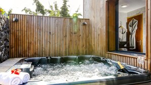 Un bain à remous avec une terrasse en bois, une serviette et une bouteille de champagne.