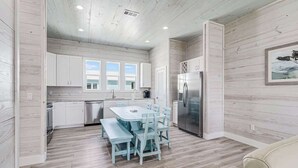 Una cocina moderna con armarios blancos, un refrigerador de acero inoxidable y una zona de comedor con una mesa y sillas azul claro.