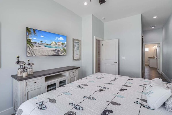 Un dormitorio con cama, escritorio, silla, televisor y puerta que da a otra habitación.